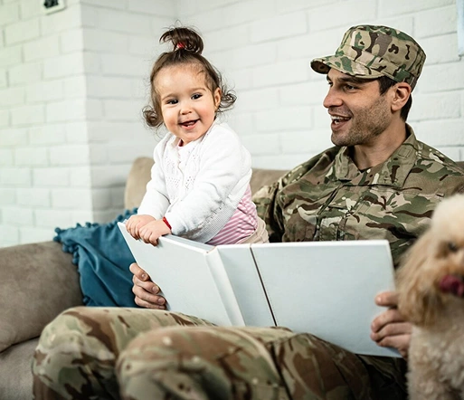 a cheerful military member reading a book to a young child while sitting on a couch